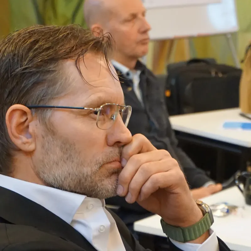 Man med glasögon lyssnar fundersamt med handen mot hakan under en workshop
